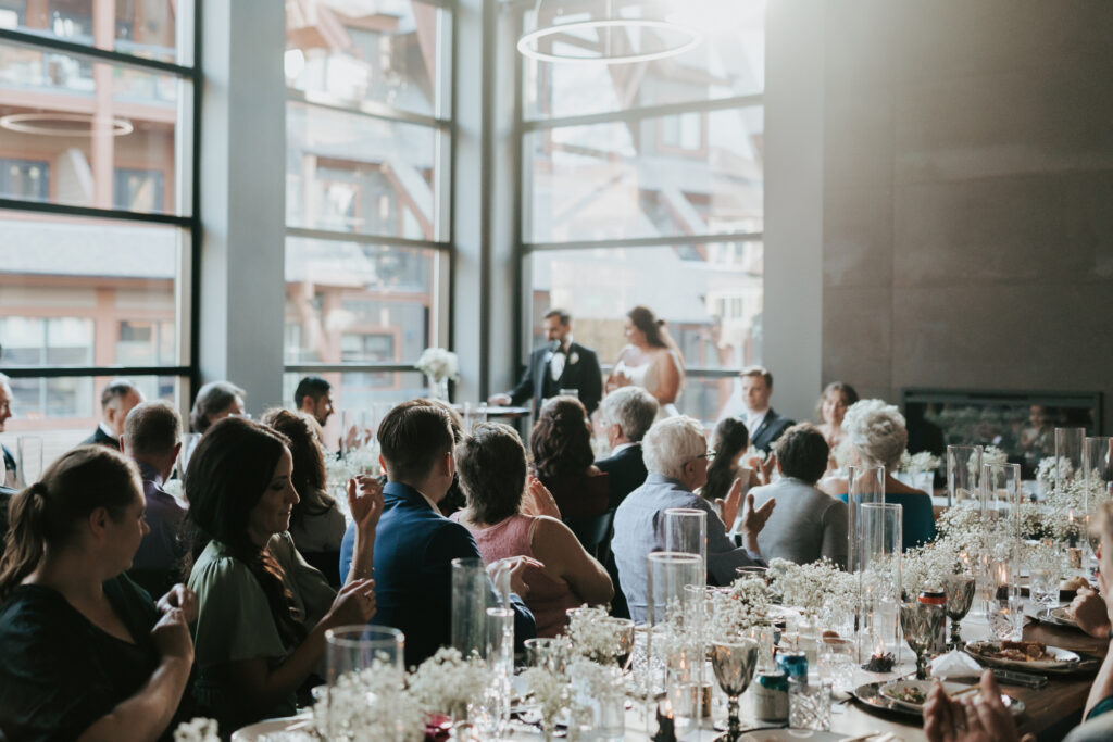 Wedding guests seated at reception tables applauding during a speech inside the Mainspace venue
