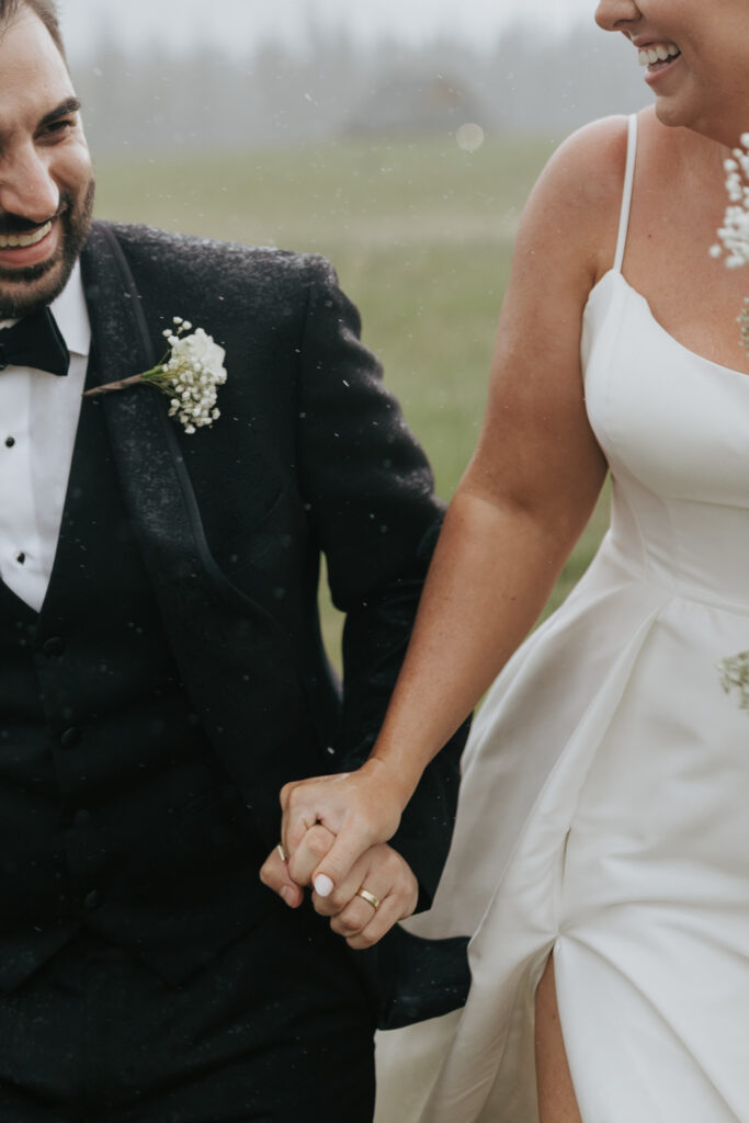 Close-up of bride and groom holding hands while walking through rain during their mountain wedding portraits