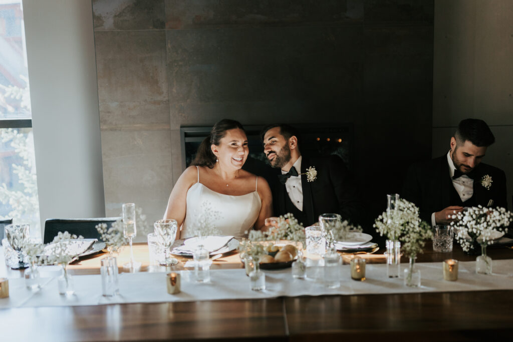 Bride and groom sitting together at their reception table surrounded by candlelight and florals