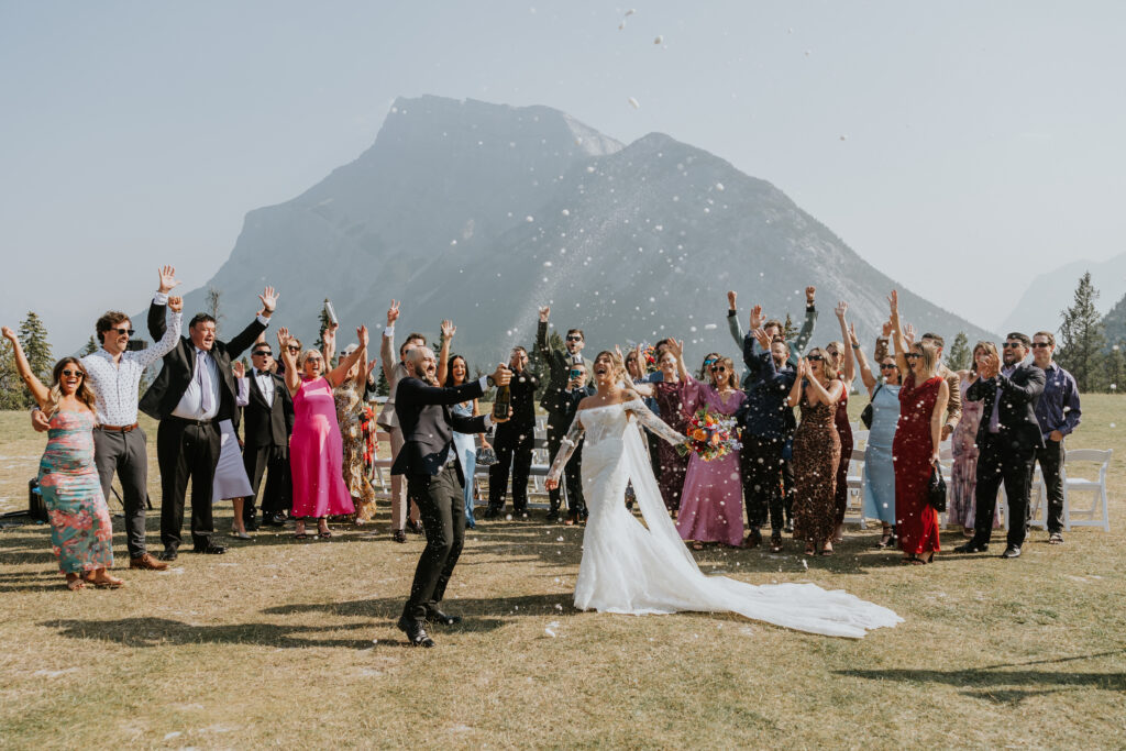 Bride spraying champagne while guests cheer around her after the ceremony