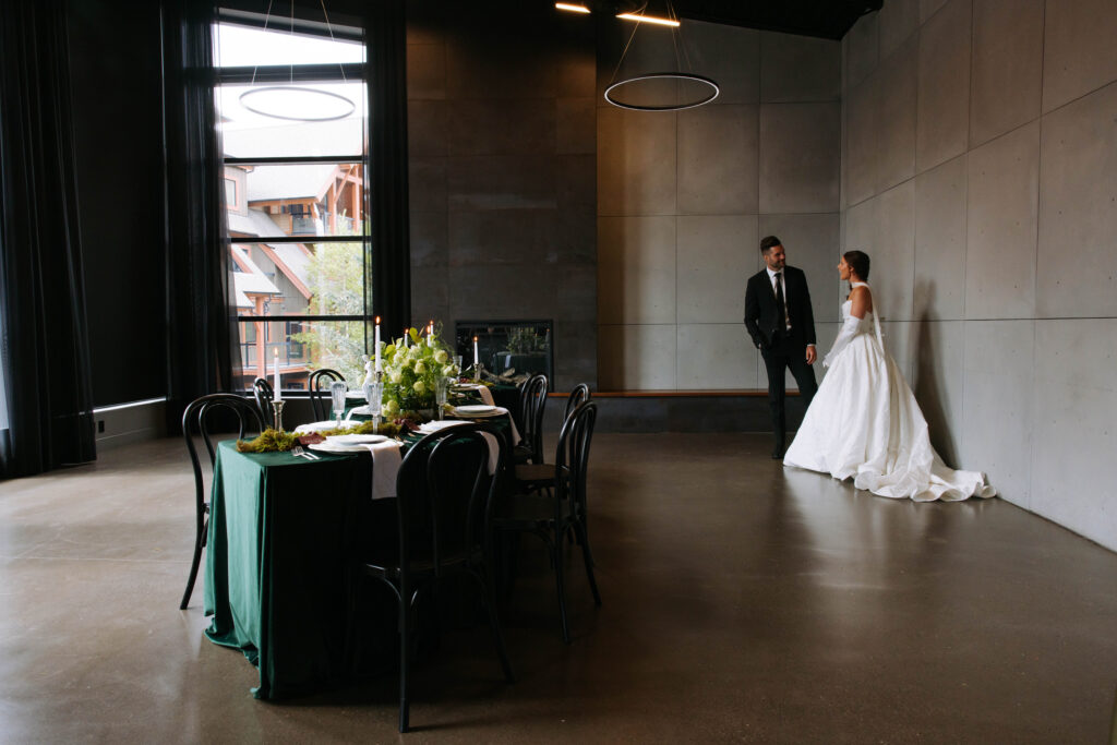 Bride and groom standing beside a styled reception table inside Mainspace with tall windows and modern concrete walls
