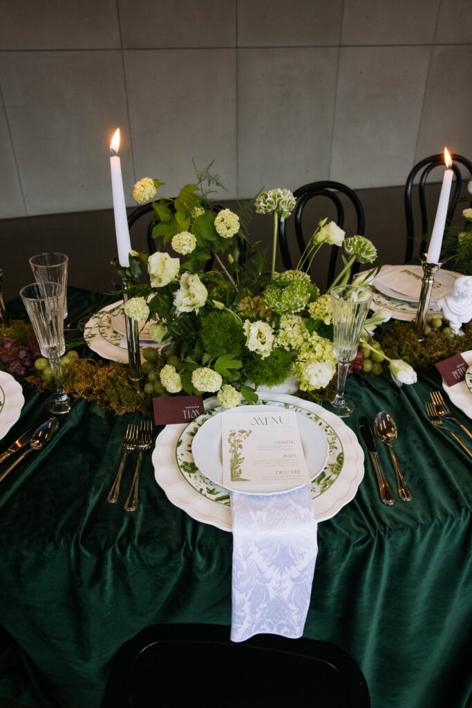 Reception table filled with green hydrangeas, candles, moss runners, and layered place settings with printed menus