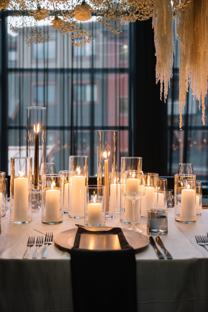 Elegant wedding reception table covered with glass candle cylinders and white candles beneath a floral hanging installation at Mainspace in Canmore
