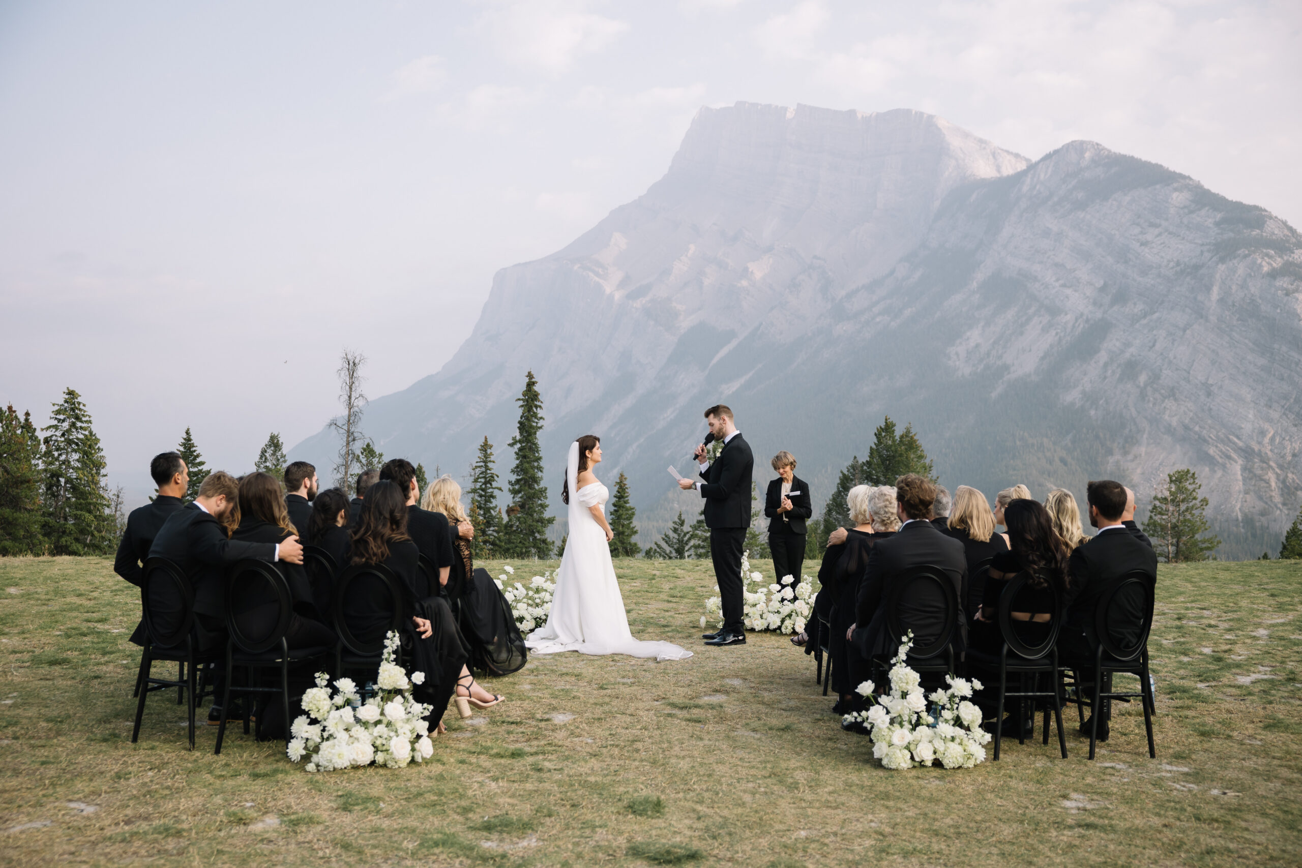 Bride and groom exchanging vows during an outdoor ceremony with guests seated and a mountain backdrop in the distance