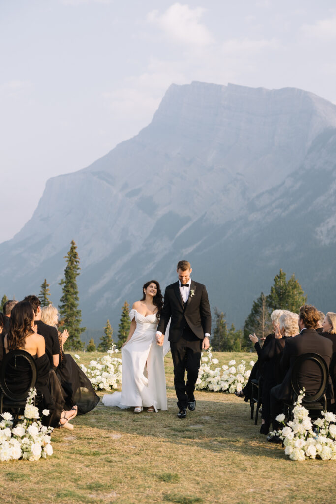 Newly married couple walking down the aisle together after their ceremony while guests celebrate around them
