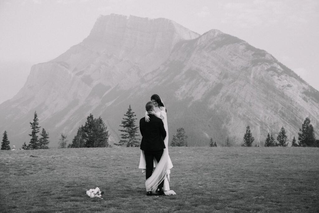 Bride and groom embracing in an open alpine field with dramatic Rocky Mountain peaks in the background