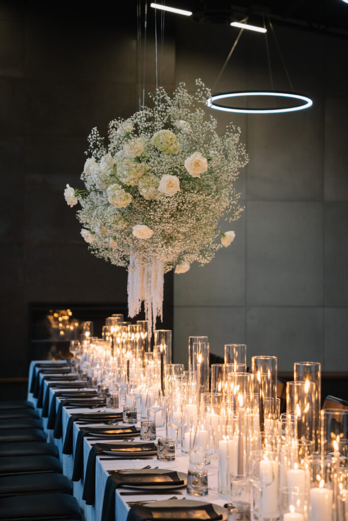 Long reception table filled with glowing candles and a tall floral centrepiece inside the modern Mainspace venue