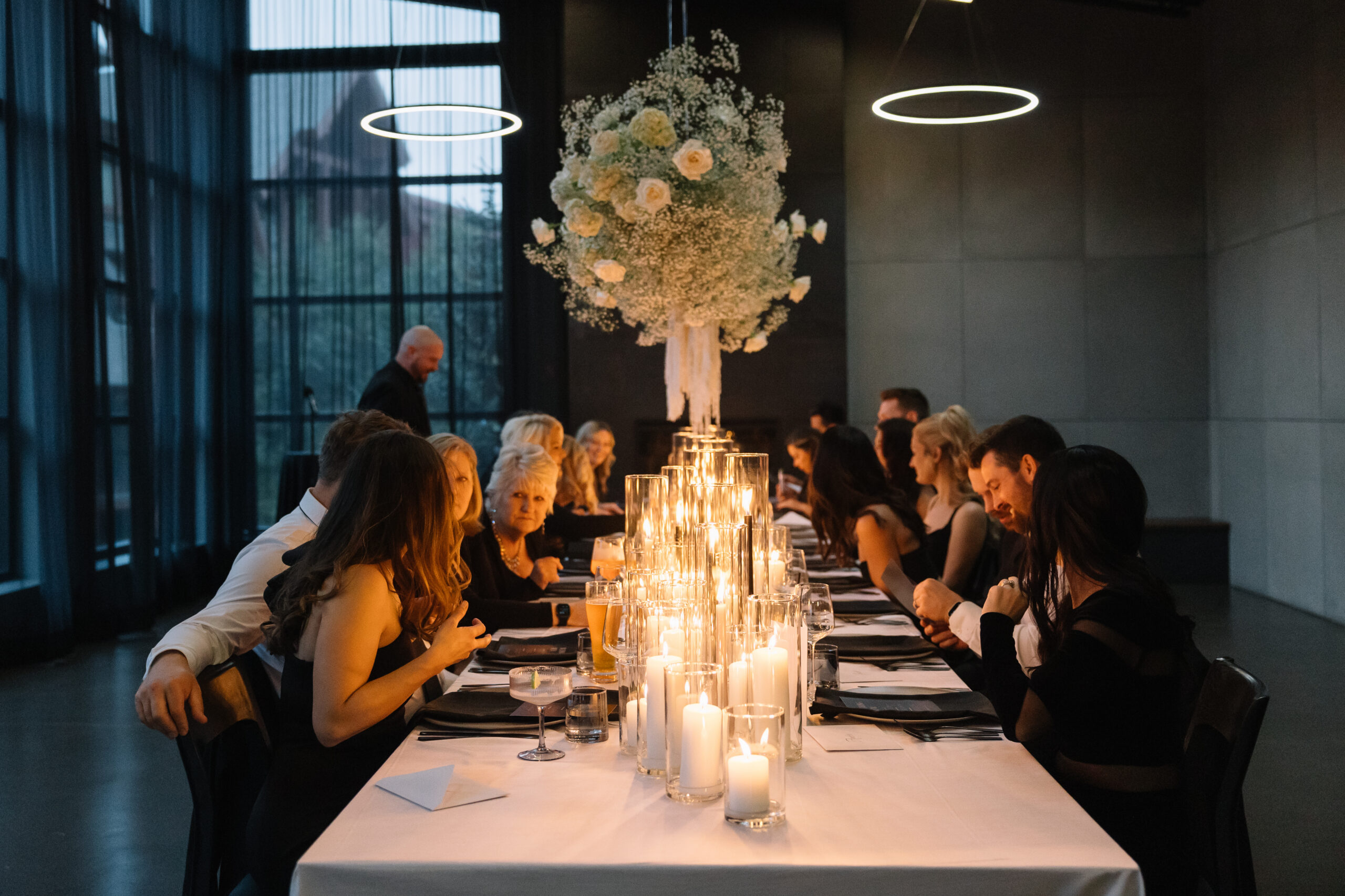 Wedding guests seated at a long candlelit reception table inside Mainspace venue in Canmore